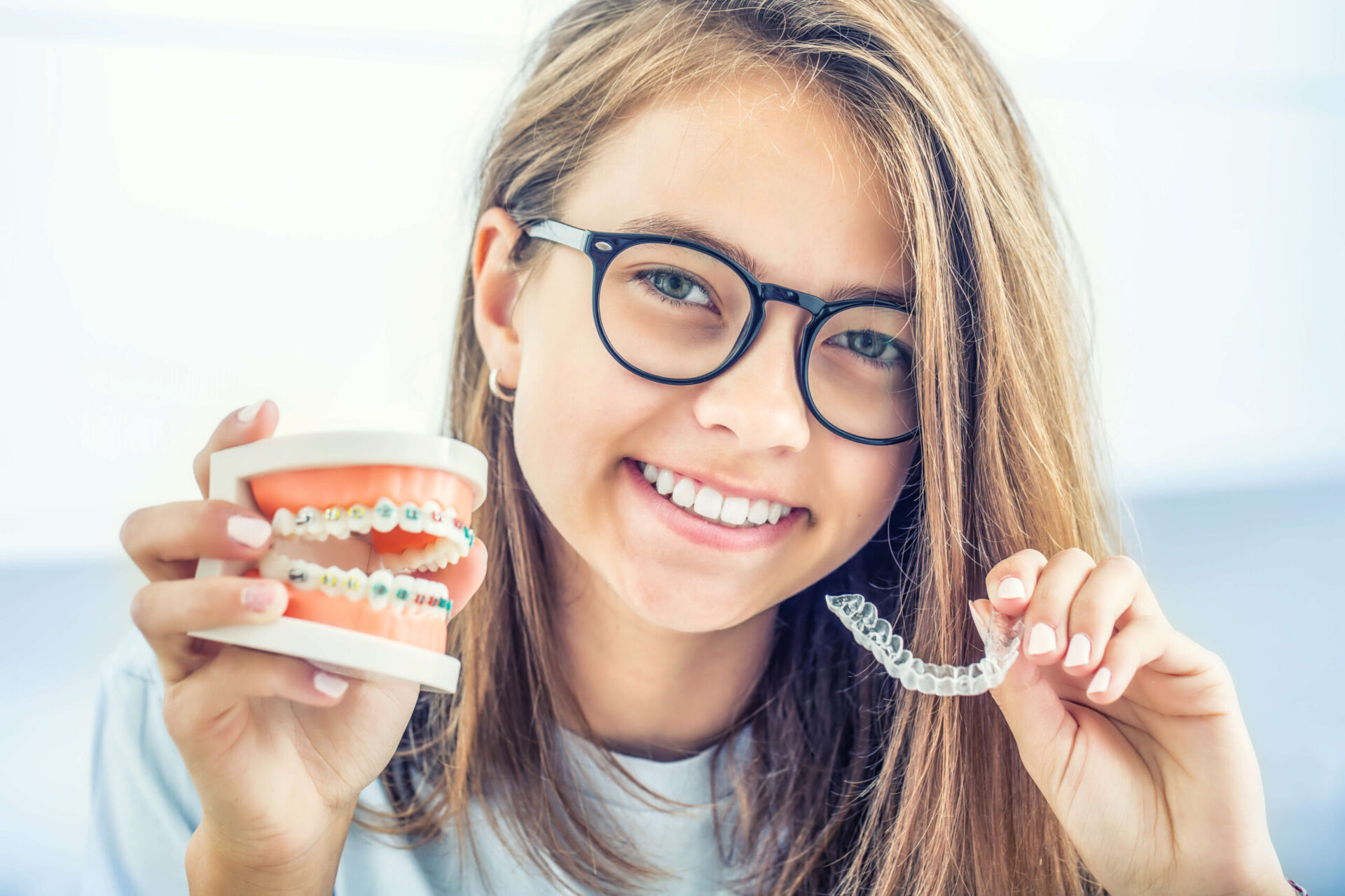 image of a smiling girl with glasses holding her new clear aligner