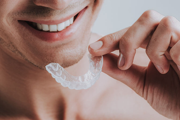 image of a man smiling while holding his clear aligner